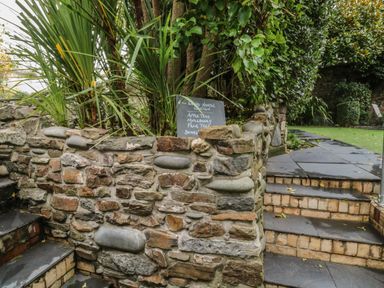 A stone wall with plants behind it and slate steps on each side leading to a garden area at Pear Tree Cottage in Appledore