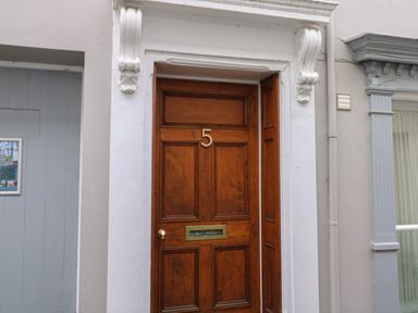 A wooden front door with the number 5 and a mail slot framed by a white decorative door surround at Pear Tree Cottage in Appledore