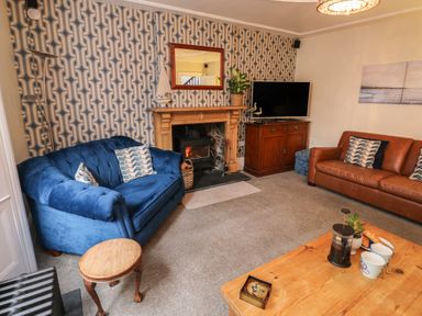 A living room with blue and brown sofas a fireplace with a wood burner and a wooden coffee table at Lands House in Appledore