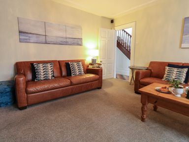 A living room with two brown leather sofas a wooden coffee table and paintings on the walls at Lands House in Appledore