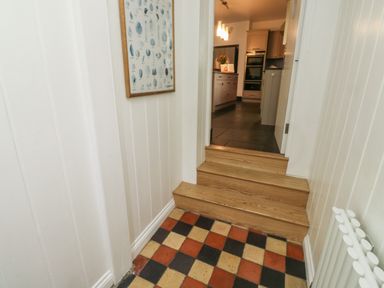 A hallway with checkerboard floor tiles leading to a kitchen with wooden steps at Lands House in Appledore