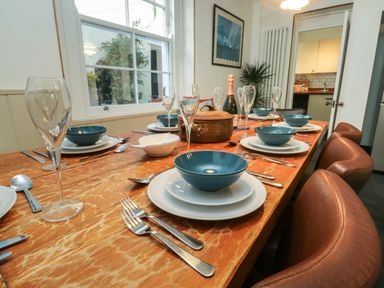 A dining table set with blue bowls white plates cutlery and glasses in a dining room at Lands House Appledore