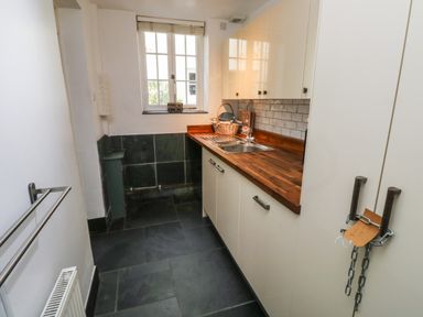 A utility room with a wooden countertop a stainless steel sink white cabinets black tiled floor and a window at Lands House in Appledore