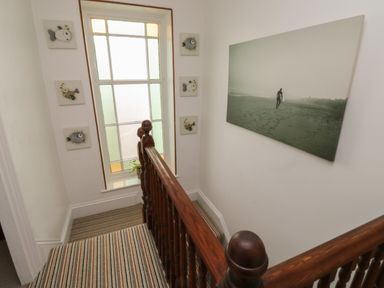 A stairway with wooden railing and striped carpet next to a large window with decorations and a wall photo at Lands House in Appledore