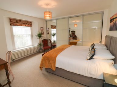 A bedroom with a bed covered in white and orange bedding next to a window and a mirrored wardrobe at Lands House in Appledore