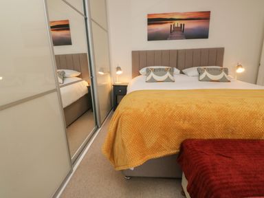 A bedroom with a large bed covered with yellow and red blankets bedside tables lamps and a wall painting at Lands House in Appledore