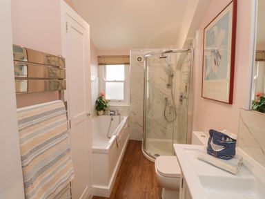 A bathroom with a bathtub, glass shower, sink, toilet, towel rack, and framed artwork at Lands House in Appledore