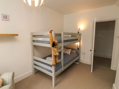 A bedroom with a gray bunk bed with blue bedding and a stuffed animal hanging on it at Lands House in Appledore