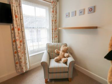 A striped armchair with a teddy bear in a room with a window and nautical curtains at Lands House in Appledore