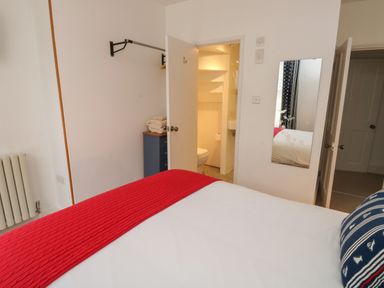 A bedroom with a bed covered by a red throw and a blue pillow with sailboat patterns at Lands House in Appledore