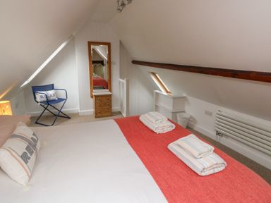A bedroom with a bed covered with white and red bedding with folded towels on it a blue chair with a pillow a standing mirror on a wooden chest of drawers and a small skylight window at Lands House in Appledore