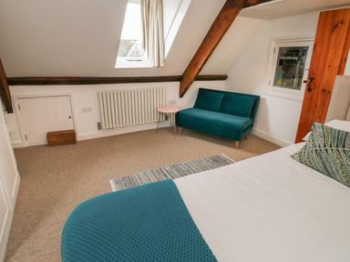 A bedroom with a bed a teal blanket a small sofa a side table and a radiator at Lands House in Appledore