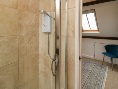 A shower with beige tiled walls and a glimpse of a room with a blue chair a rug and a skylight window at Lands House in Appledore