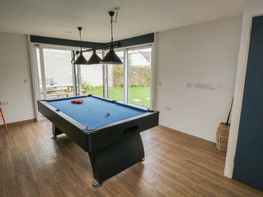 A room with a pool table and hanging lights overlooking a garden at Lands House in Appledore