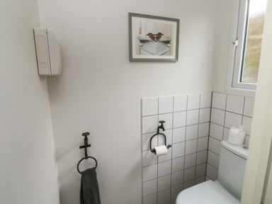 A bathroom with a toilet a window a towel ring with a towel a toilet paper holder and a framed picture of a dog at Lands House in Appledore