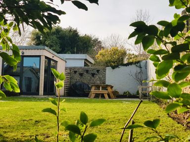 A backyard with green grass a wooden picnic table a shed and a stone wall at Lands House in Appledore