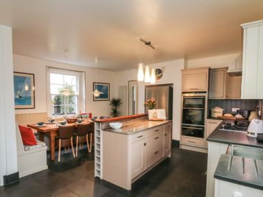 A kitchen with an island counter a dining area with a table and chairs and built in bench seating at Lands House in Appledore