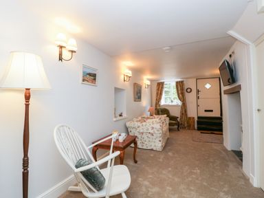 A living room with a white rocking chair a floral sofa a green armchair and a wall mounted television at The Old Thatch in Porlock