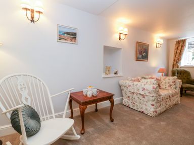 A sitting room with a white rocking chair a wooden table with teacups a floral sofa and green armchair at The Old Thatch in Porlock