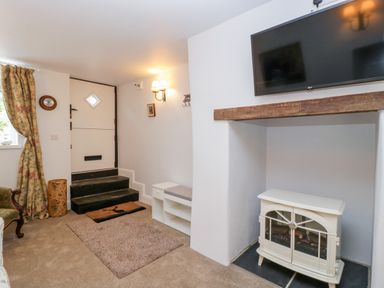 A room with a white door and steps a wall-mounted tv above a fireplace and a cushioned bench near the door at The Old Thatch Porlock