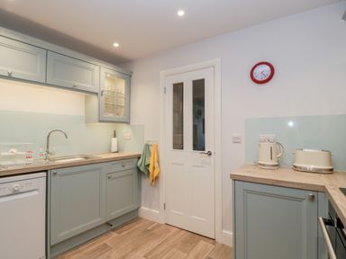 A kitchen with a sink dishwasher cupboards a clock kettle and toaster at The Old Thatch in Porlock