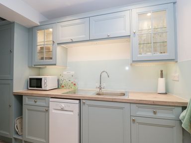 A kitchen with blue cabinets a countertop a sink a microwave and a dishwasher at The Old Thatch in Porlock
