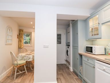 A kitchen and dining area with light blue cabinets a microwave a dishwasher and a small table with chairs at The Old Thatch in Porlock