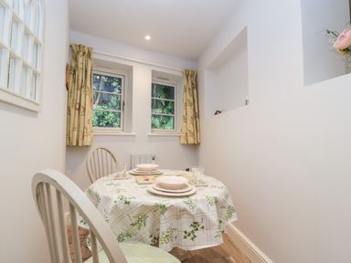 A small dining area with a round table and two chairs near two windows with curtains at The Old Thatch in Porlock