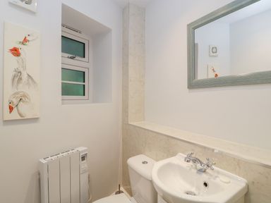 A bathroom with a sink and toilet below a large mirror and a window with frosted glass at The Old Thatch in Porlock