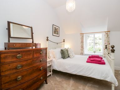 A bedroom with a wooden chest of drawers a white metal bed with pillows and pink towels by a window at The Old Thatch in Porlock