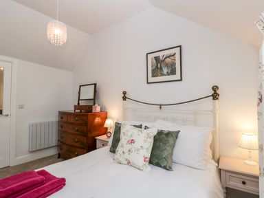 A bedroom with a bed with floral and green pillows a wooden chest of drawers with a mirror and two bedside tables with lamps at The Old Thatch in Porlock