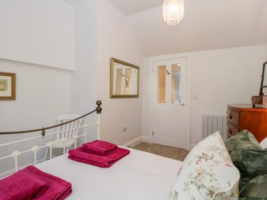 A bedroom with a white metal bed with pink towels on it a wooden dresser a white chair and a mirror on the wall at The Old Thatch in Porlock