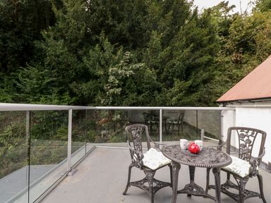 An outdoor patio with a metal table and two chairs with cushions overlooking trees at The Old Thatch in Porlock