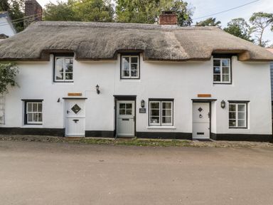 A white thatched cottage with three doors and windows along a street at The Old Thatch in Porlock