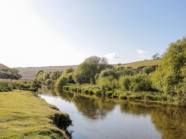 A river flowing through green fields and trees under a clear sky at The Old Thatch in Porlock