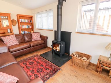 A living room with brown leather sofas a wood burning stove and a basket with firewood at Gloccamaura in Bovey Tracey