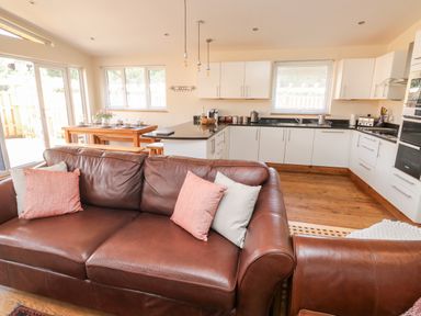 An open plan kitchen and living area with brown leather sofas and a wooden dining table at Gloccamaura in Bovey Tracey