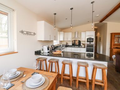 A kitchen with a breakfast bar with wooden stools and a dining table set with dishes at Gloccamaura in Bovey Tracey