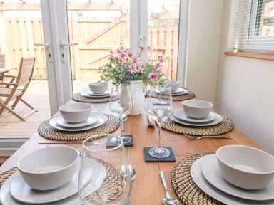 A dining table set with white bowls plates wine glasses and a flower vase near glass doors at Gloccamaura in Bovey Tracey