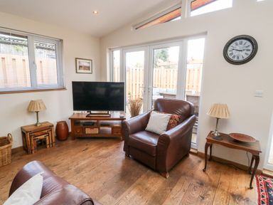 A living room with leather chairs a TV wooden floors side tables and a clock on the wall at Gloccamaura in Bovey Tracey