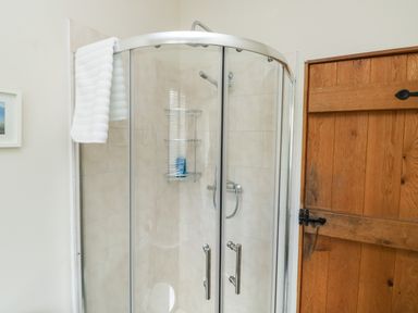 A corner glass shower enclosure with tiled walls a white towel hanging and a wooden door at Gloccamaura in Bovey Tracey