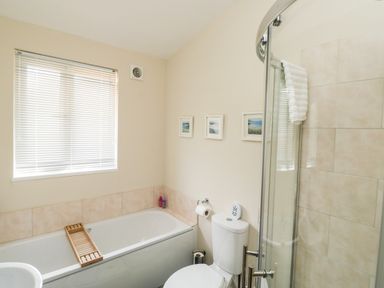 A bathroom with a bathtub wooden tray a toilet with a toilet paper holder a glass shower enclosure and three framed pictures on the wall at Gloccamaura in Bovey Tracey