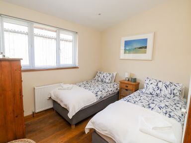 A bedroom with two single beds with patterned bedding a wooden chest of drawers a window and a bedside table at Gloccamaura in Bovey Tracey