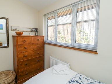 A bedroom with a wooden chest of drawers beside a bed under a window with blinds at Gloccamaura in Bovey Tracey