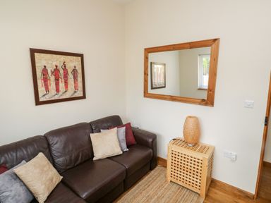 A brown leather sofa with cushions a framed painting a wooden framed mirror and a wooden stand with a lamp at Gloccamaura in Bovey Tracey