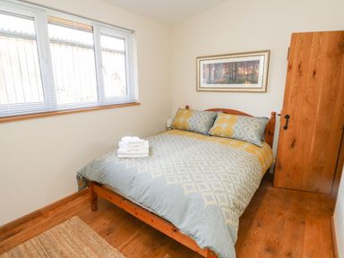A bedroom with a bed with patterned bedding and folded towels on it a window with blinds a wooden floor a wooden door and a framed picture on the wall at Gloccamaura in Bovey Tracey