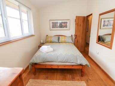 A bedroom with a double bed wooden furniture a window with blinds and a wall mirror at Gloccamaura in Bovey Tracey