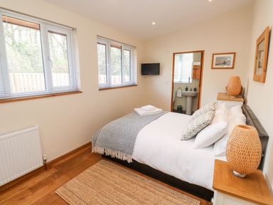 A bedroom with a double bed two lamps on bedside tables a rug and an ensuite bathroom at Gloccamaura in Bovey Tracey