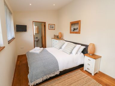 A bedroom with a double bed flanked by two nightstands a wall-mounted TV and an ensuite bathroom at Gloccamaura in Bovey Tracey