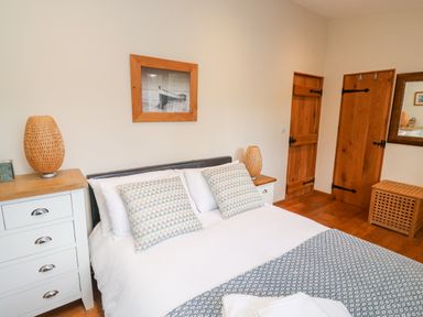 A bedroom with a made bed pillows bedside tables lamps wooden doors and a mirror at Gloccamaura in Bovey Tracey